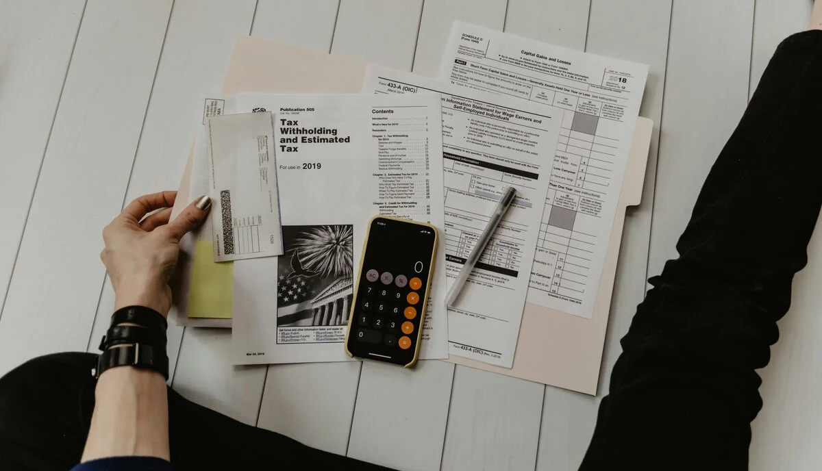 Person using calculator with retirement planning documents and financial charts, planning for future financial security